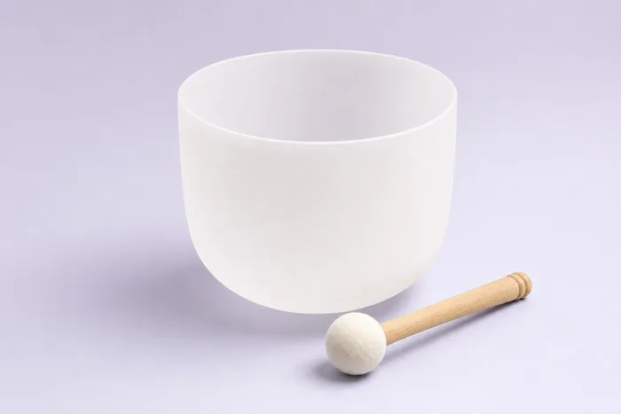 A single frosted quartz singing bowl with its mallet on a lavender studio background